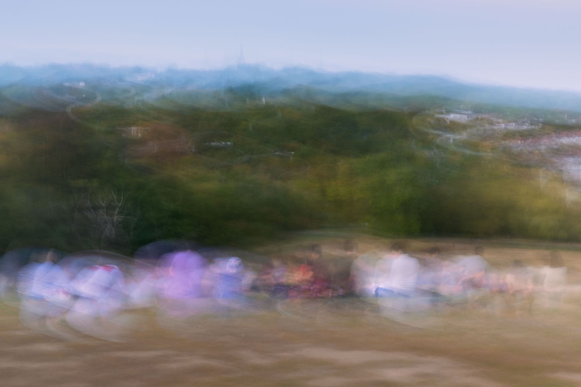 A crowd blurred into a band of color beneath green hills and a pale sky