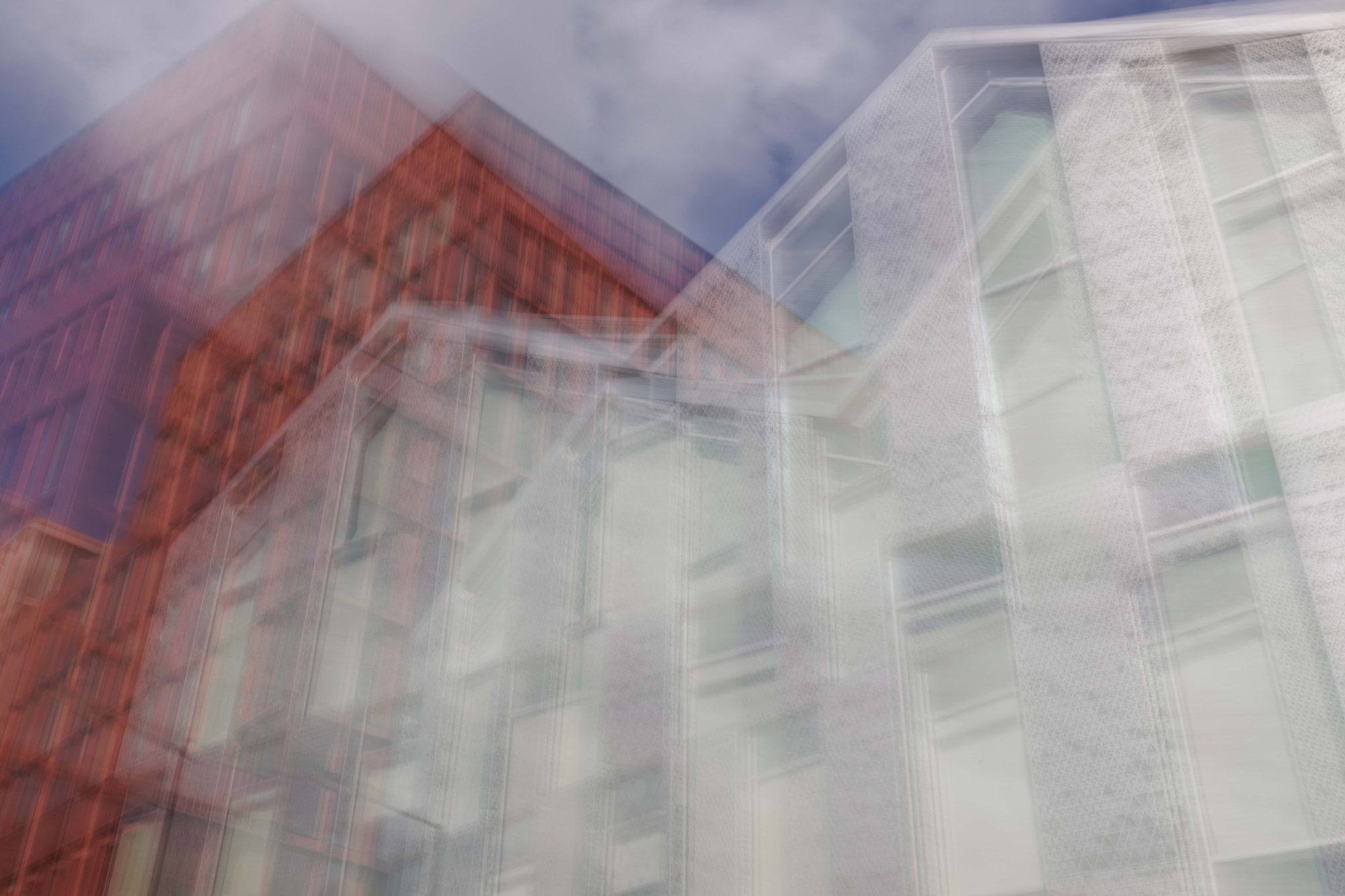 Red brick and white perforated façades blurring together against a cloudy blue sky