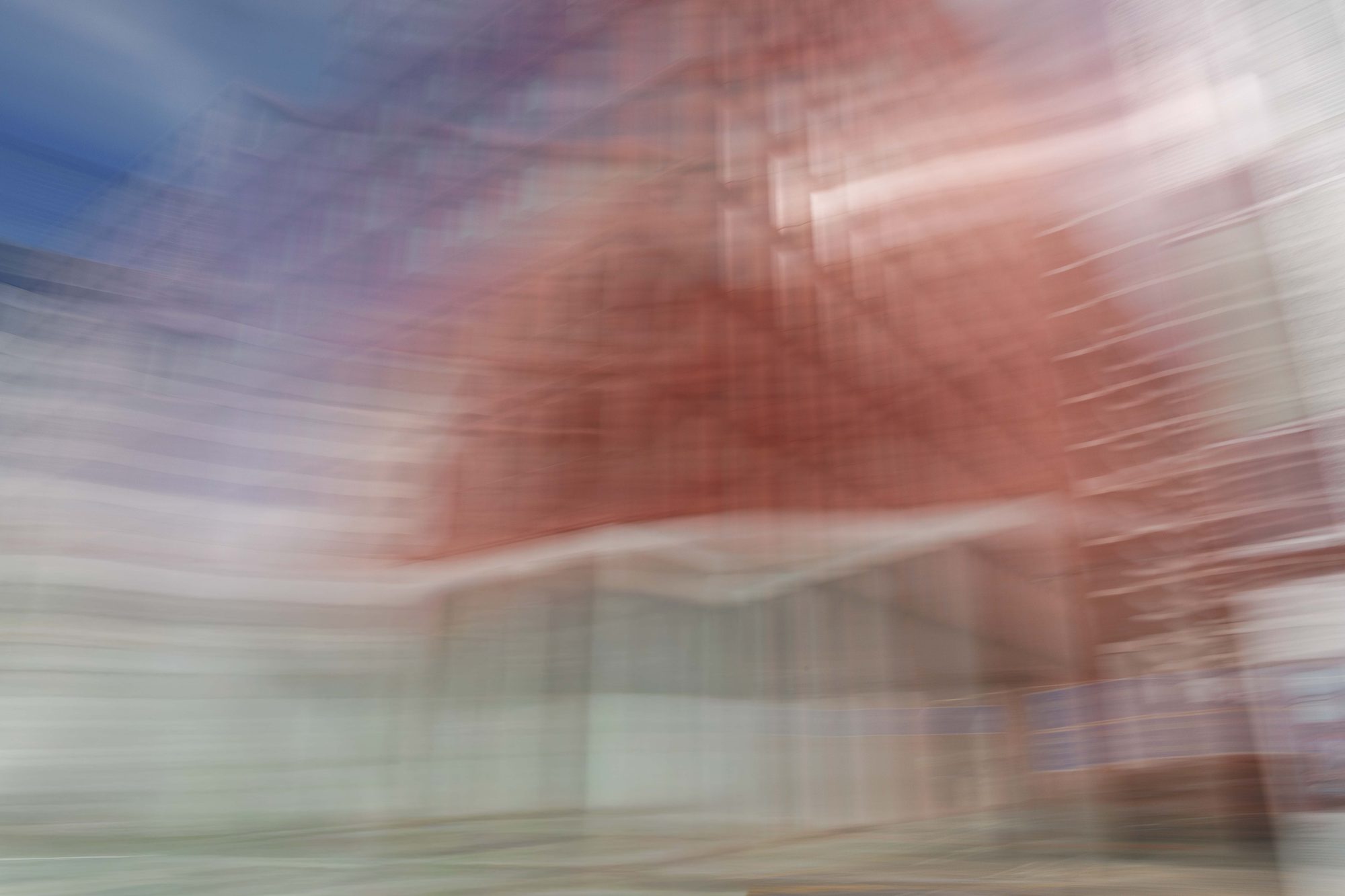 A red building dissolving into sweeping streaks of white, blue, and gray