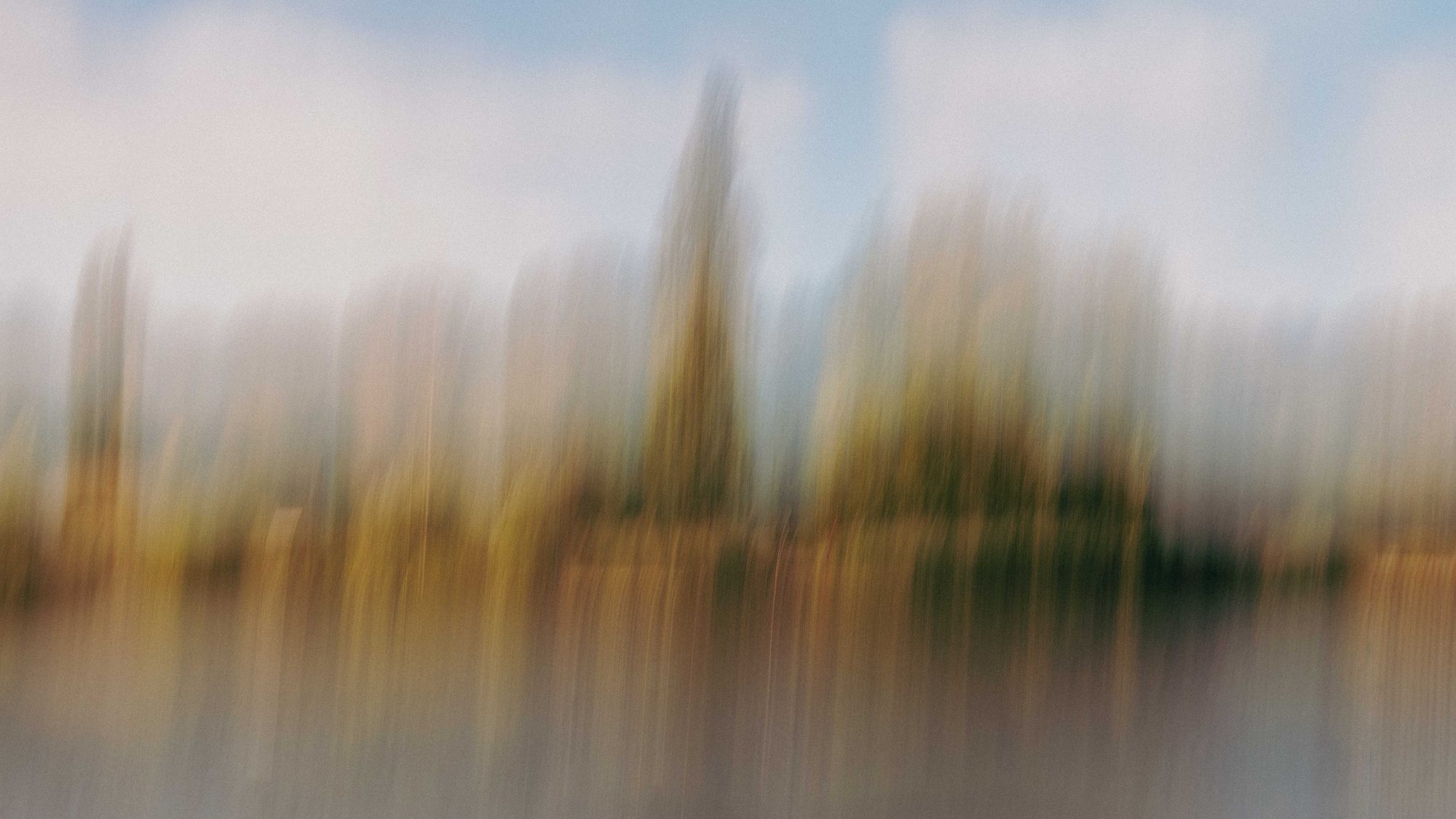 A pale treeline and slender spire mirrored in still water
